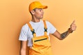 Young handsome african american man wearing handyman uniform over yellow background looking proud, smiling doing thumbs up gesture Royalty Free Stock Photo