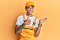 Young handsome african american man wearing handyman uniform over yellow background showing palm hand and doing ok gesture with Royalty Free Stock Photo