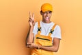 Young handsome african american man wearing handyman uniform over yellow background smiling with happy face winking at the camera Royalty Free Stock Photo