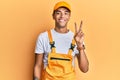 Young handsome african american man wearing handyman uniform over yellow background smiling looking to the camera showing fingers Royalty Free Stock Photo