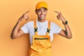 Young handsome african american man wearing handyman uniform over yellow background smiling pointing to head with both hands Royalty Free Stock Photo