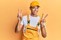 Young handsome african american man wearing handyman uniform over yellow background smiling with tongue out showing fingers of Royalty Free Stock Photo