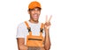 Young handsome african american man wearing handyman uniform smiling with happy face winking at the camera doing victory sign Royalty Free Stock Photo