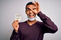 Young handsome african american man wearing medical mask holding virus alert reminder with happy face smiling doing ok sign with Royalty Free Stock Photo