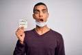 Young handsome african american man wearing medical mask holding virus alert reminder scared in shock with a surprise face, afraid Royalty Free Stock Photo