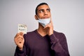 Young handsome african american man wearing medical mask holding virus alert reminder serious face thinking about question, very Royalty Free Stock Photo