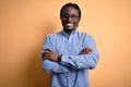 Young handsome african american man wearing shirt and glasses over yellow background happy face smiling with crossed arms looking Royalty Free Stock Photo