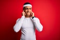 Young handsome african american sportsman wearing sportswear over red background covering ears with fingers with annoyed