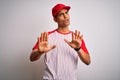 Young handsome african american sportsman wearing striped baseball t-shirt and cap Moving away hands palms showing refusal and