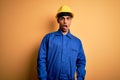 Young handsome african american worker man wearing blue uniform and security helmet In shock face, looking skeptical and Royalty Free Stock Photo