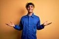 Young handsome african american worker man wearing blue uniform and security helmet smiling showing both hands open palms, Royalty Free Stock Photo