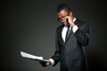 Young handsome african businessman in grey costume, white shirt, tie and glasses standing and reading paper documets