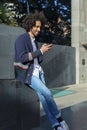 Young handsome African man using his smartphone with smile while sitting on a bench outdoors in sunny day Royalty Free Stock Photo