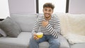 Young, handsome arab man exuding confidence enjoying his morning cup of coffee, smiling joyfully while comfortably sitting on a Royalty Free Stock Photo