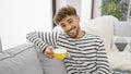 Young, handsome arab man exuding confidence enjoying his morning cup of coffee, smiling joyfully while comfortably sitting on a Royalty Free Stock Photo