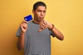 Young handsome arab man holding credit card standing over isolated yellow background with angry face, negative sign showing Royalty Free Stock Photo