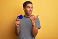 Young handsome arab man holding credit card standing over isolated yellow background pointing and showing with thumb up to the Royalty Free Stock Photo