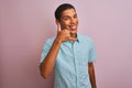 Young handsome arab man wearing blue shirt standing over isolated pink background smiling doing phone gesture with hand and Royalty Free Stock Photo