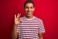 Young handsome arab man wearing striped t-shirt over isolated red background smiling positive doing ok sign with hand and fingers Royalty Free Stock Photo