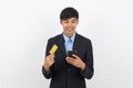 Young handsome asian business man holding a black smartphone,credit card while smiling isolated on white background. Royalty Free Stock Photo