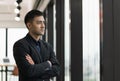 Young handsome asian businessman in suit standing near window with arm crossed in office Royalty Free Stock Photo