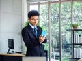 Young handsome Asian businessman in suit using mobile phone in office Royalty Free Stock Photo