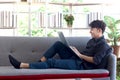 Young handsome Asian man in black shirt typing on keyboard laptop computer while lying down comfortably on sofa couch in his Royalty Free Stock Photo