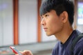 Young handsome asian man looking forward while using cellphone checking social media, surfing internet, and mobile apps at weekend Royalty Free Stock Photo