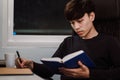 Young handsome asian man reading book and writing note at work desk late at night.