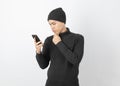 Young handsome asian man wearing grey sweater and beanie while playing smartphone with doubts face on white background. Royalty Free Stock Photo