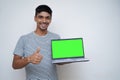 Young handsome asian teen boy showing thumbs up with a laptop on the other hand with a green screen Royalty Free Stock Photo