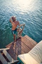 Young handsome athletic man in swimsuit shorts comming out of water, up on ladder to wooden jetty. Man on summer vacation by sea. Royalty Free Stock Photo