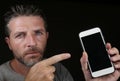 Young handsome and attractive Caucasian man holding mobile phone in his hand pointing it with the finger isolated on black Royalty Free Stock Photo