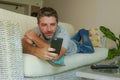 Young handsome attractive happy man using online dating app on mobile phone networking with smartphone lying at home couch Royalty Free Stock Photo