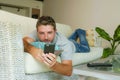 Young handsome attractive happy man using online dating app on mobile phone networking with smartphone lying at home couch Royalty Free Stock Photo