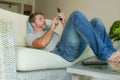 Young handsome attractive happy man using online dating app on mobile phone networking with smartphone lying at home couch Royalty Free Stock Photo