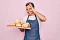 Young handsome baker man with blue eyes wearing apron holding tray with homemade bread with happy face smiling doing ok sign with