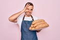 Young handsome baker man with blue eyes wearing apron holding tray with wholmeal bread with happy face smiling doing ok sign with Royalty Free Stock Photo