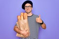 Young handsome baker man with blue eyes wearing french beret holding bag with bread happy with big smile doing ok sign, thumb up Royalty Free Stock Photo