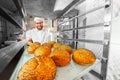 A young handsome baker takes fresh hot buns with poppy seeds from the oven in front of the bakery