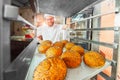 A young handsome baker takes fresh hot buns with poppy seeds from the oven in front of the bakery