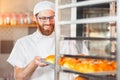 A young handsome baker takes out hot fresh baking from the oven in the bakery