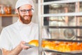 A young handsome baker takes out hot fresh baking from the oven in the bakery