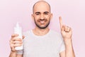 Young handsome bald man holding bottle of cream lotion smiling with an idea or question pointing finger with happy face, number Royalty Free Stock Photo