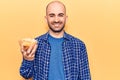 Young handsome bald man holding bowl with potato chips looking positive and happy standing and smiling with a confident smile Royalty Free Stock Photo