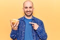 Young handsome bald man holding bowl with potato chips smiling happy pointing with hand and finger Royalty Free Stock Photo