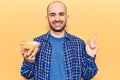 Young handsome bald man holding bowl with potato chips smiling happy pointing with hand and finger to the side Royalty Free Stock Photo