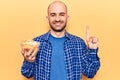 Young handsome bald man holding bowl with potato chips smiling with an idea or question pointing finger with happy face, number Royalty Free Stock Photo