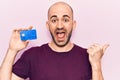 Young handsome bald man holding credit card pointing thumb up to the side smiling happy with open mouth Royalty Free Stock Photo