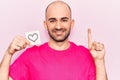 Young handsome bald man holding reminder with heart shape smiling with an idea or question pointing finger with happy face, number Royalty Free Stock Photo